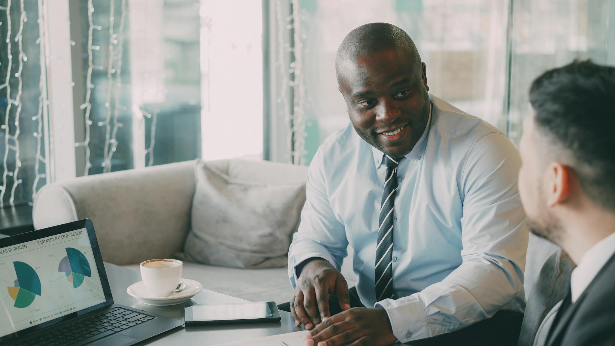 Two businessmen discussing projects over coffee and data charts.